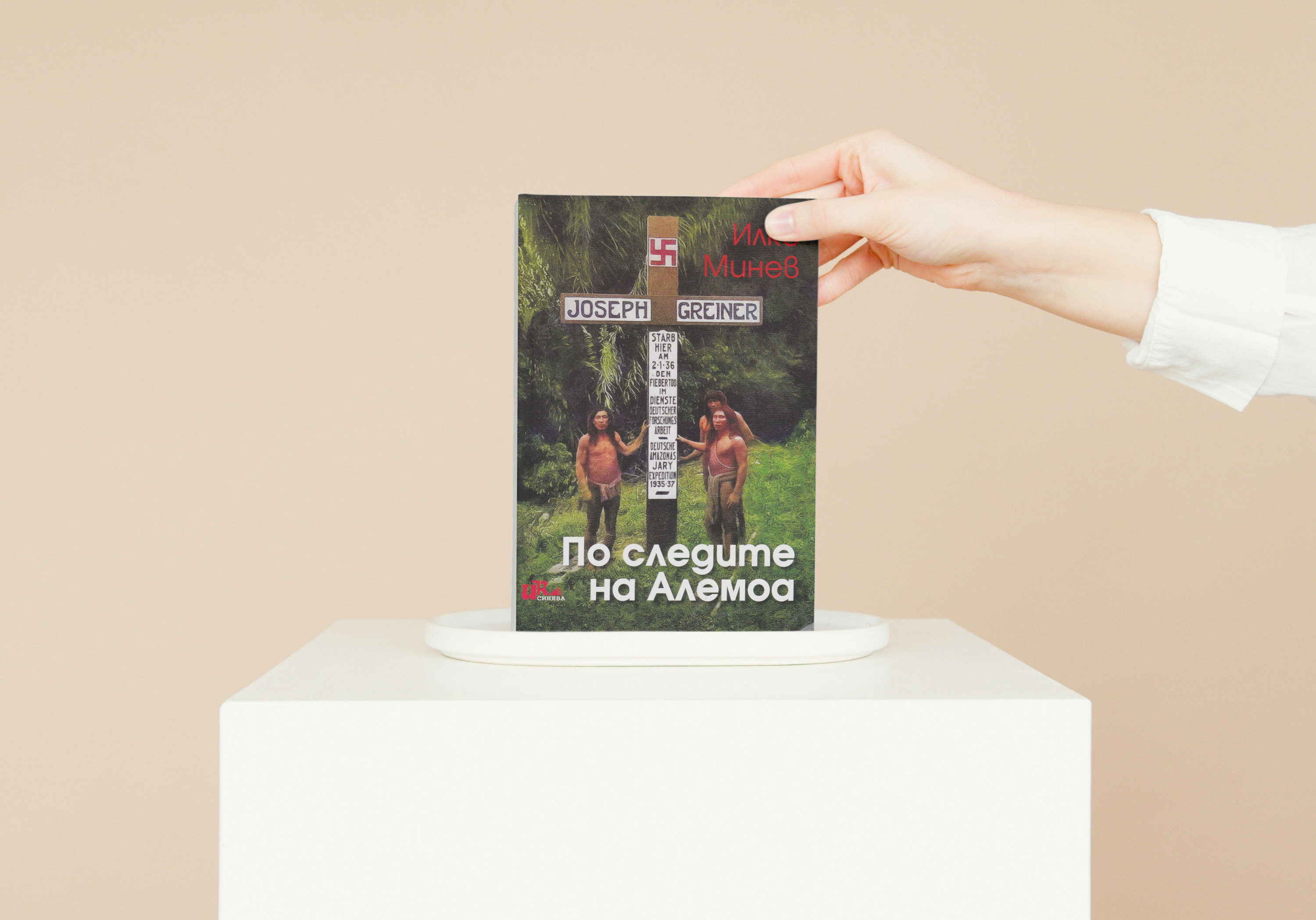 Човек държи книга със заглавие „По следите на Алемоа“ върху поставка